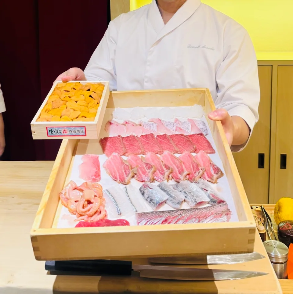 A chef presenting a wooden tray of fish and sea urchin